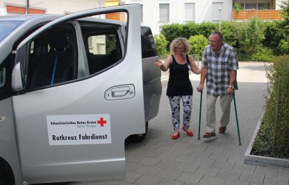 Freiwillige Rotkreuz-Fahrerin holt Fahrgast zu Hause ab und fährt ihn zur Therapie.